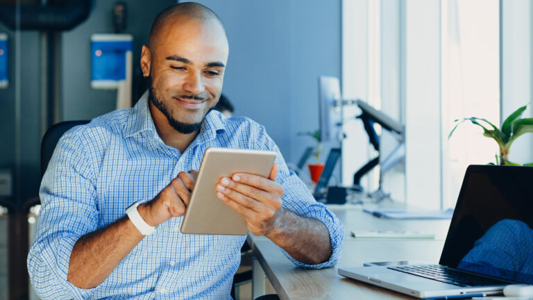 A man at his work desk looking at his iPad to access Watts' Online Training program. A Learn 